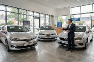Intérieur d'une concession automobile française avec plusieurs voitures hybrides exposées sur sol béton poli et vendeur en costume marine